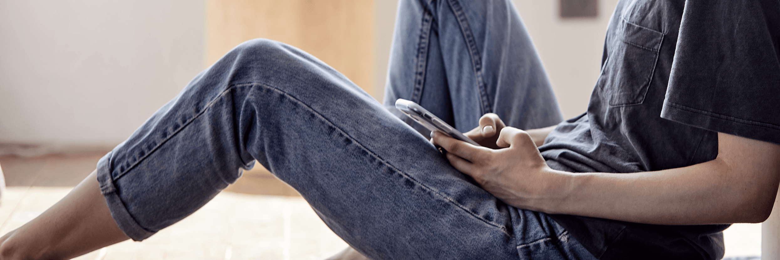Zbliżenie na ręce postaci, która siedzi pod ścianą i trzyma w ręku telefon
