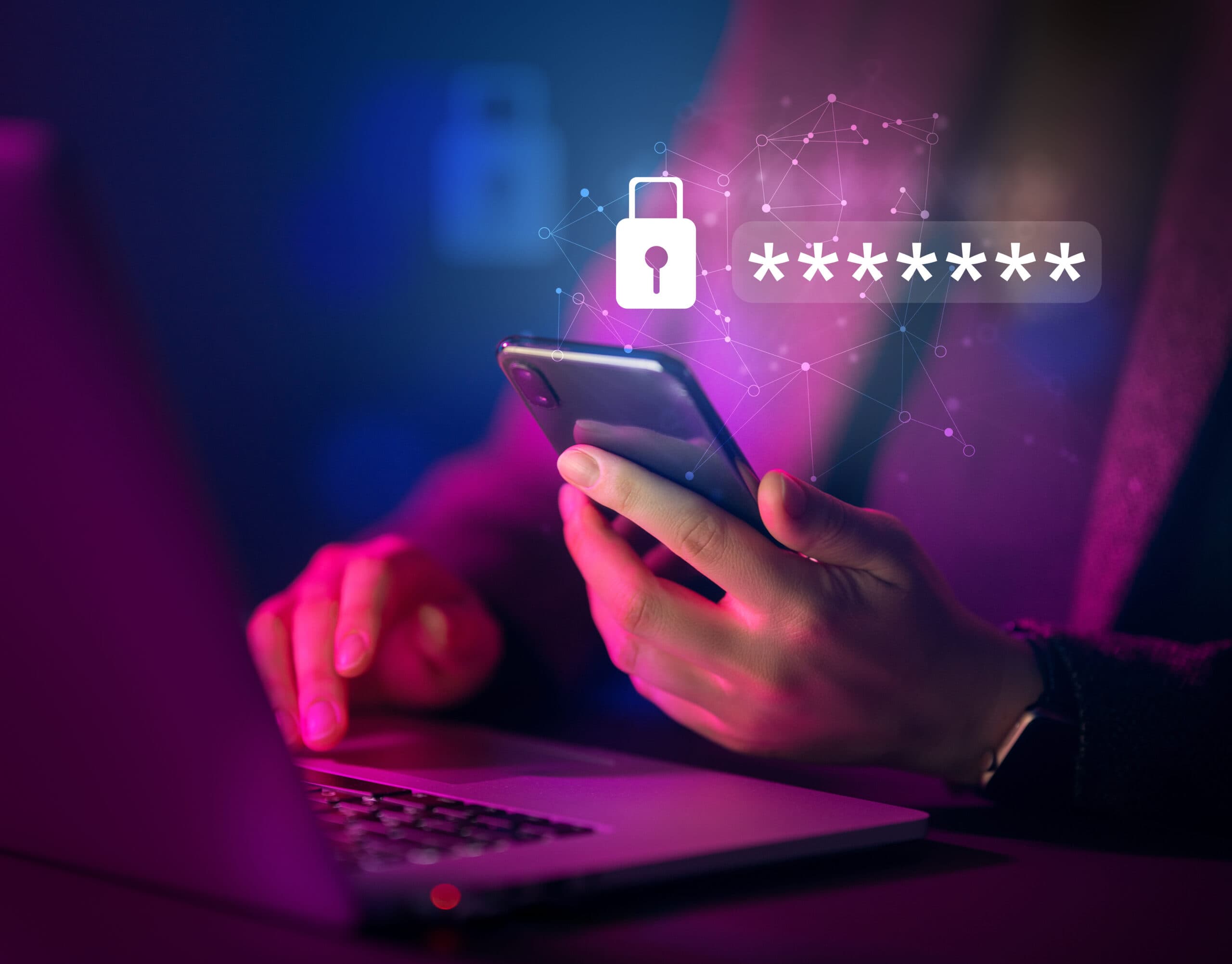 Osoba trzymająca smartfon w ręku, pracująca na laptopie w ciemnym, nastrojowym oświetleniu. Na zdjęciu widoczna jest ikona kłódki oraz symbol gwiazdek reprezentujących hasło, co podkreśla tematykę bezpieczeństwa danych i cyberochrony.