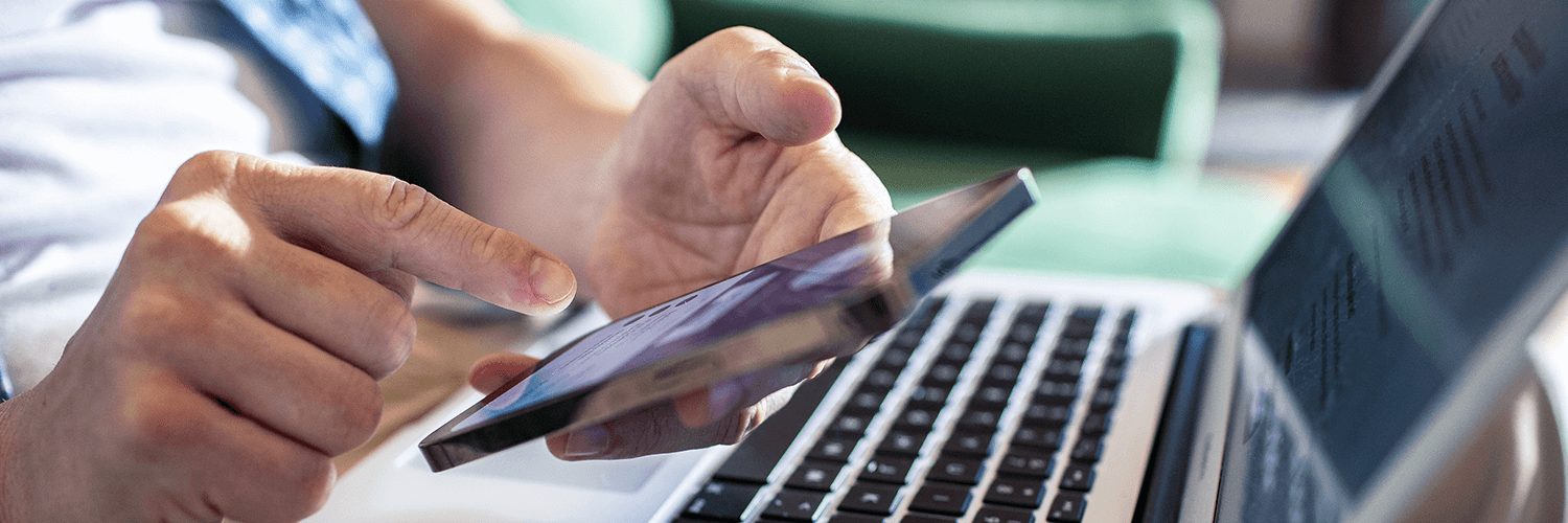 Kobieta trzymająca w ręku telefon i mająca za nim otwarty laptop