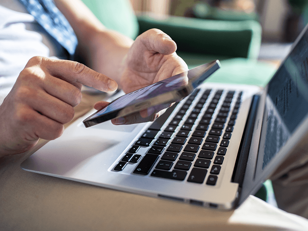 Kobieta trzymająca w ręku telefon i mająca za nim otwarty laptop