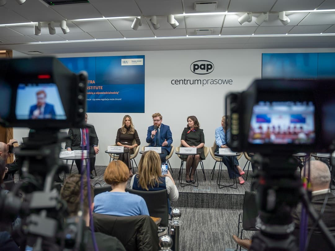 Panel dyskusyjny w centrum prasowym PAP. Na scenie Małgorzata Rozenek-Majdan, Iwona Prószyńska i Dariusz Standerski. Standerski mówi do mikrofonu. Widać kamery nagrywające wydarzenie i publiczność na sali.