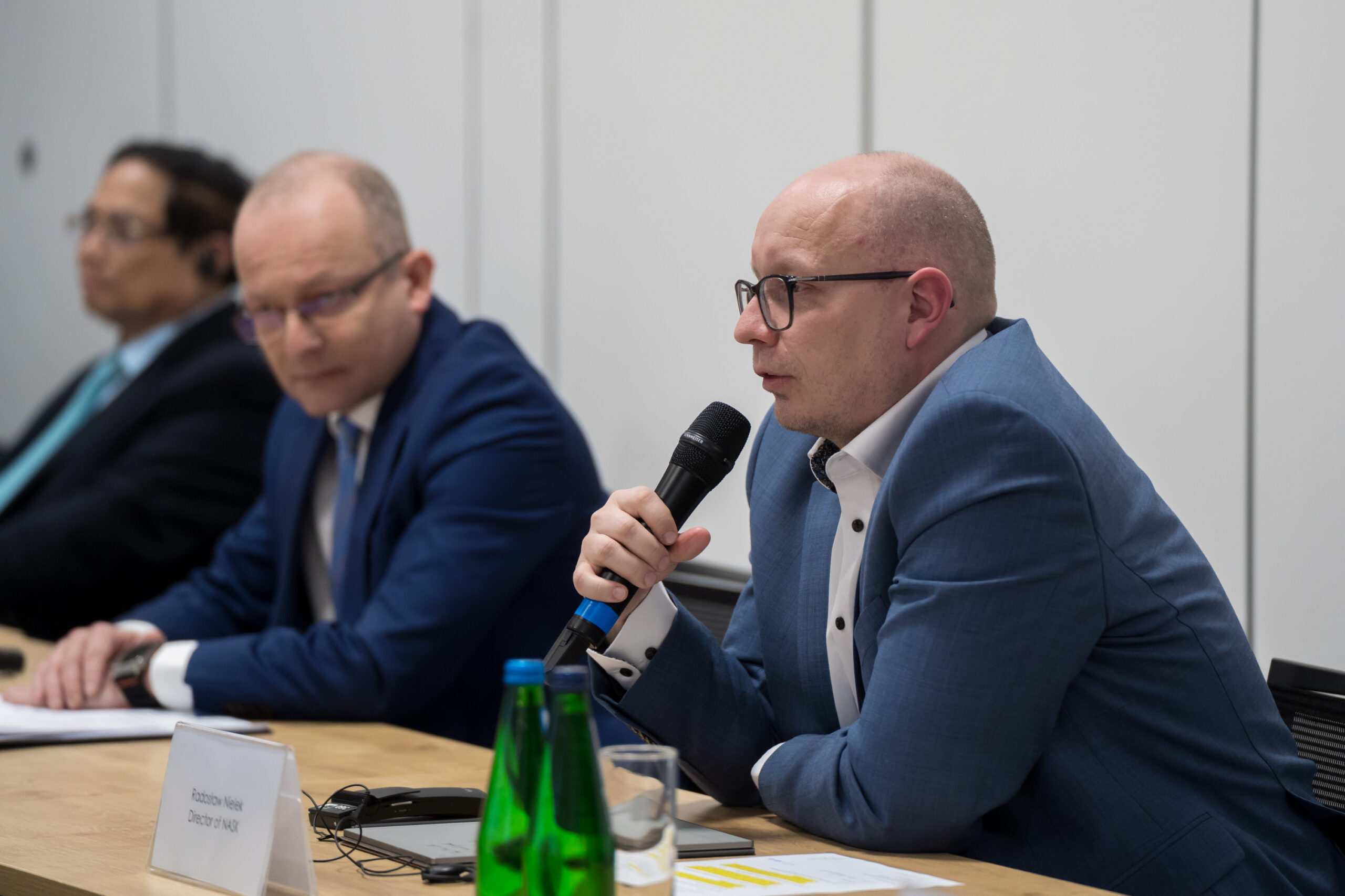 Dyrektor NASK, Radosław Nielek, siedzi przy stole i przemawia do mikrofonu. Obok niego, w tle, widoczny jest Paweł Olszewski, sekretarz stanu w Ministerstwie Cyfryzacji, oraz Premier Wietnamu Phạm Minh Chính.